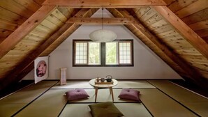 Ein traditioneller Raum mit Tatami-Matten, Holzboden und einer Holzzielung, einem Tatami-Tisch, zwei Kissen und einer Hängelampe.