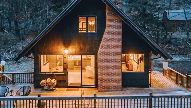 Eine Holzhütte mit großem Glasflurtür, einem Ziegelkamin und einer Terrasse mit Stühlen.