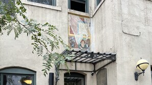 Een gebouwtoegang met een zwarte deur, een klein bakstenen bouwwerk links en een groen bord waarop staat dat roken niet is toegestaan binnen 7,5 meter van de ingangen.