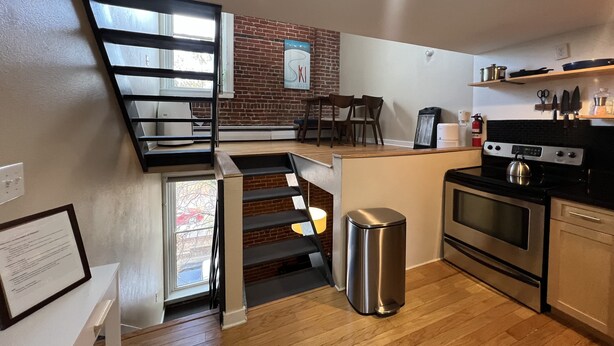 Een compacte keuken met een moderne kookplaat, een prullenbak en een eethoek met stoelen.