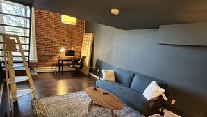 Een woonkamer met een bakstenen muur, een blauwe bank, een houten salontafel en een kamerkleed met een patroon.