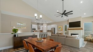A modern kitchen with white cabinets, a dining area with a wooden table and orange chairs, and a living area with a beige sofa and a flat-screen TV mounted above a fireplace. - The Liftview: 3BR home at Purgatory Resort (Durango)