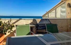 Enjoy the ocean view from this balcony, featuring a grill, two chairs, and a potted plant.