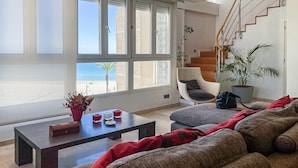 Ein modernes Wohnzimmer mit einem großen Fenster, einer Treppe und Blick auf den Strand.