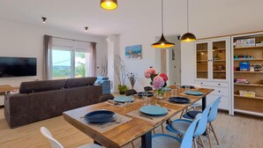 A modern living room with a sofa, dining table, and chairs. There is a TV mounted on the wall, a window with a view, and a cabinet with items on it. - Pet friendly home in Pula (Pula)