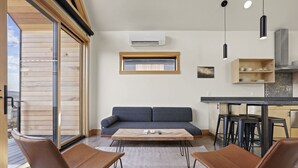Una sala moderna con sofá, dos sillones, una mesa de centro y una cocina con taburetes.