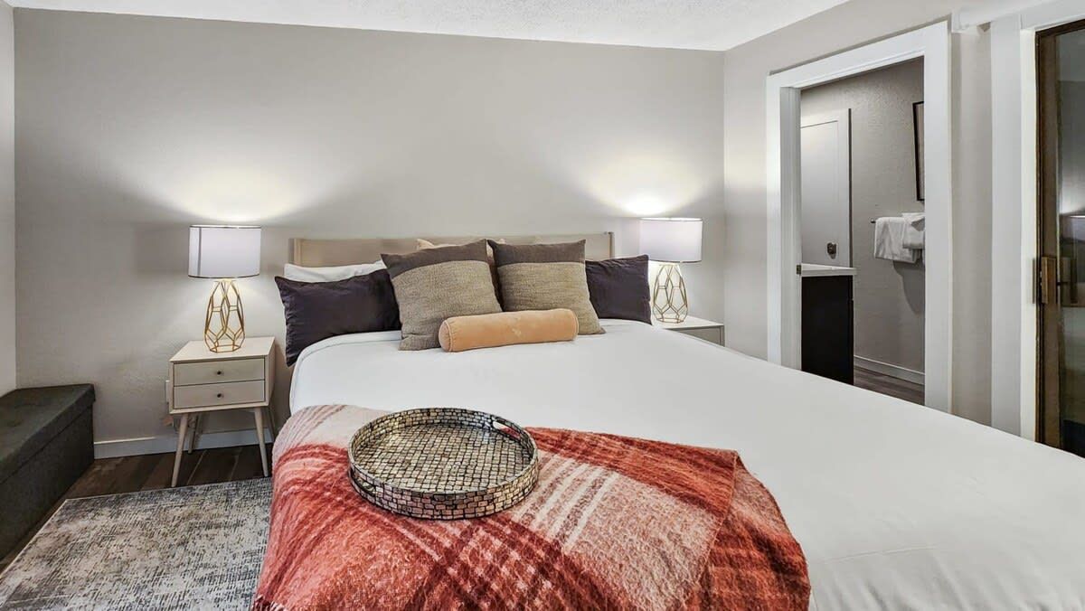 Ein Hotelzimmer mit einem Bett, Nachttischen, einer Lampe, einem Korb und einem Kleiderschrank.