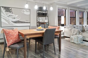 Ein modernes Wohnzimmer mit Essbereich, ausgestattet mit einem Holztisch, Stühlen, einer Couch und einem großen abstrakten Gemälde.