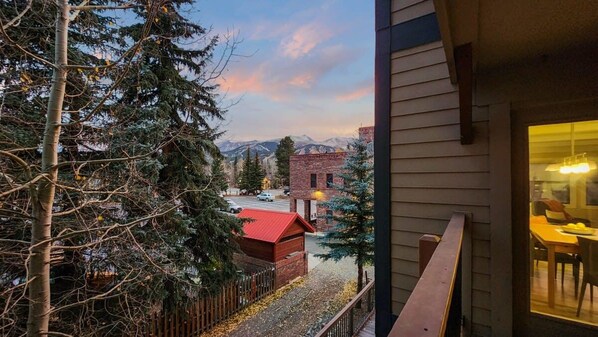 A balcony with a view of a mountain range, a red-roofed building, and a wooden fence.