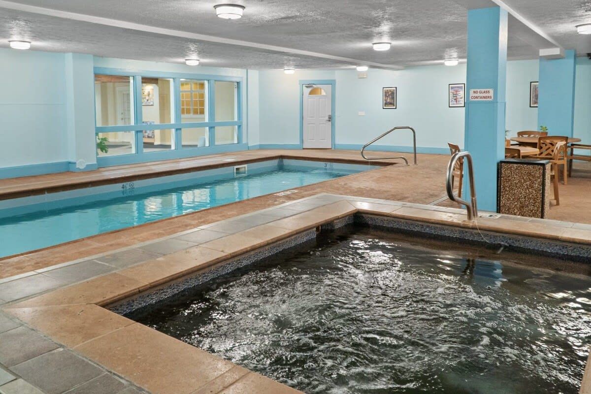An indoor swimming pool with a diving board, a changing room, and a seating area with tables and chairs.