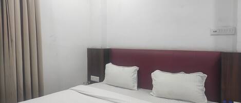 A hotel room with a bed, two pillows, a nightstand with water bottles, and a power outlet.
