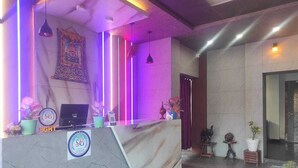 A reception desk with a marble top, a logo, and a computer. There are plants and a small table with a vase. - Hotel SG Hub Tower (Tinsukia)