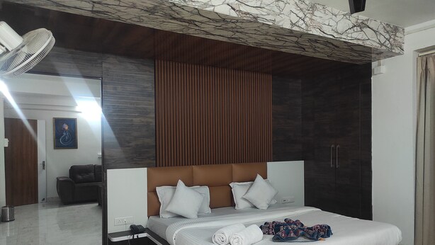 A modern bedroom with a large bed, a wooden headboard, a mirror, and a ceiling with a marble-like design. - Hotel SG Hub Tower (Tinsukia)