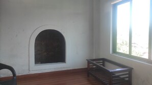 A room with a wooden floor, a white wall with a small arched window, and a large window with a view of greenery outside. - Hotel SG Hub Tower (Tinsukia)