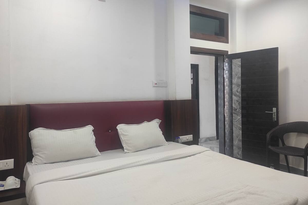A hotel room with a bed, a nightstand, a chair, and a door leading to another room.