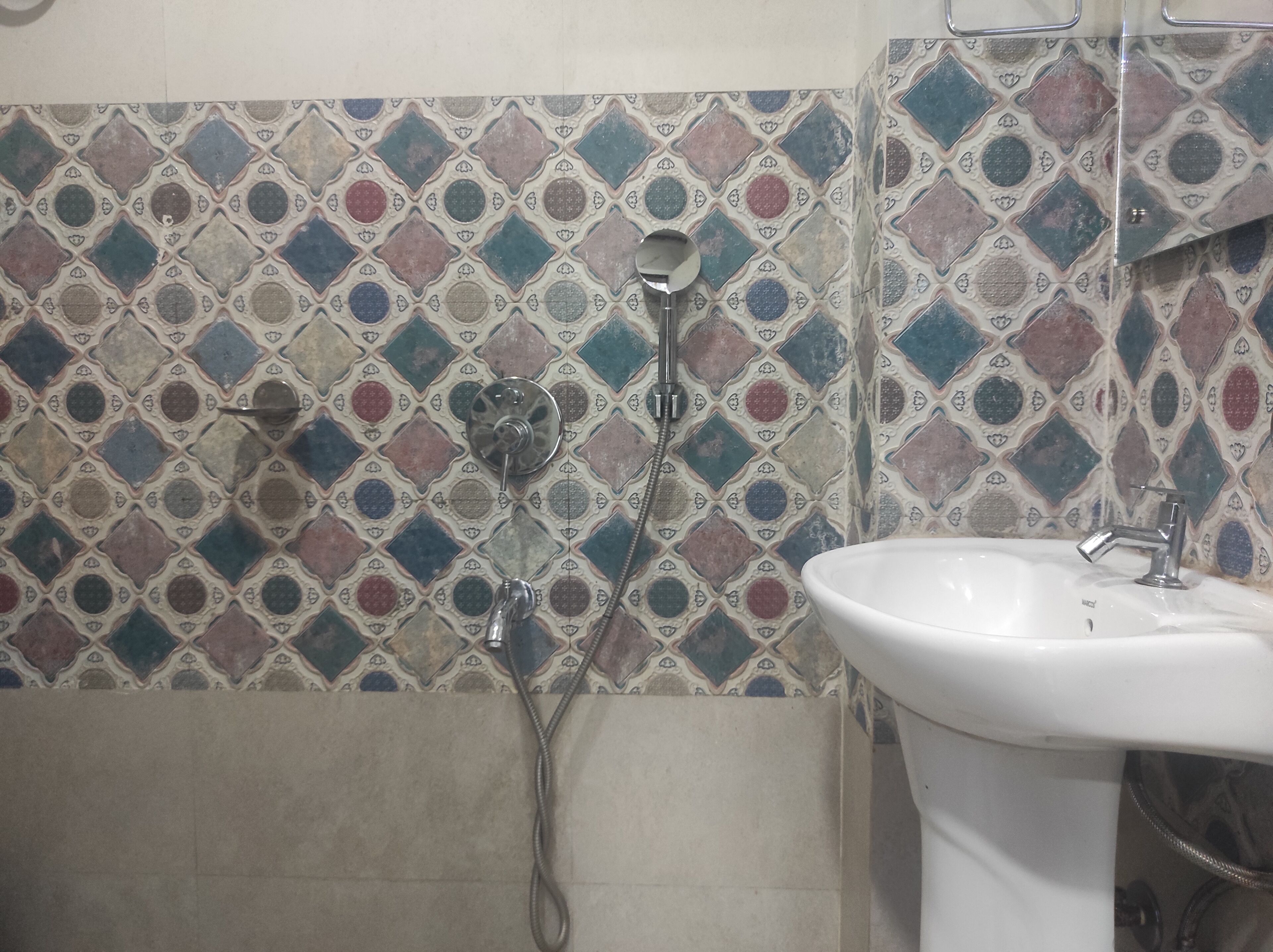 A bathroom with a tiled wall featuring a geometric pattern, a white sink, and a shower with a handheld showerhead.