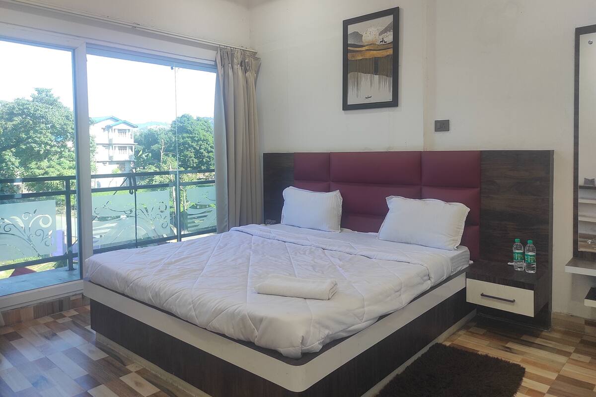 A bedroom with a large bed, a view of a balcony, and a painting on the wall.
