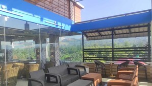 An outdoor seating area with wicker furniture and a glass enclosure overlooking a mountainous landscape. - Hotel SG Hub Tower (Tinsukia)