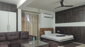 A modern hotel room with a sofa, a glass coffee table, a bed with a headboard, a ceiling fan, and a window with curtains. - Hotel SG Hub Tower (Tinsukia)