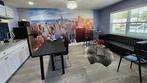 Uma cozinha moderna com área de jantar, apresentando um mural da paisagem urbana, uma mesa de jantar preta e um sofá preto.