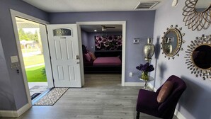 Quarto com porta para uma varanda, uma cadeira roxa e espelhos decorativos nas paredes.