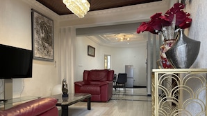 Un moderno salón con un sofá de cuero rojo, una mesa de centro de vidrio, un televisor de pantalla plana y un jarrón decorativo con flores rojas.