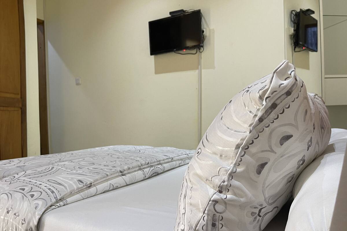 A hotel room with a bed, a television mounted on the wall, and a door.