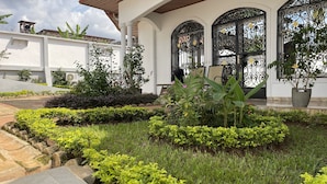 Un jardín bien cuidado con diversas plantas y un edificio blanco con puertas arqueadas.
