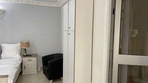 Un dormitorio con una cama, una mesita de noche, una lámpara, una silla negra y un armario.