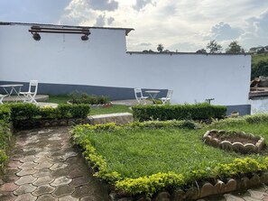 Un jardín en la azotea con sillas y mesas blancas, rodeado de follaje y un camino empedrado.