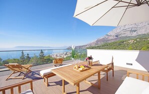 A wooden deck with a table set for dining, a lounge chair, and an umbrella. - Amazing home in Makarska (Makarska)