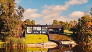 Ein modernes Haus mit großen Glasfenstern, einem Rasen und einem Teich.