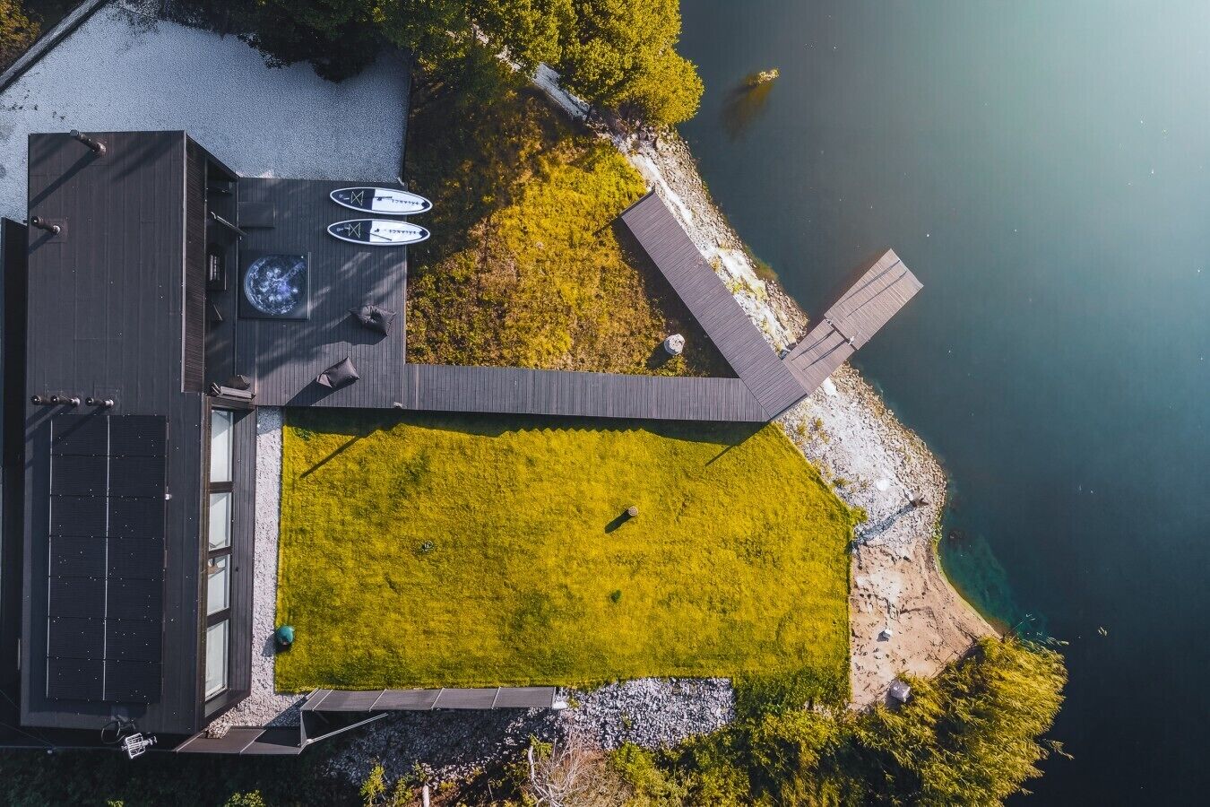 Vue aérienne d’une maison moderne dotée d’une terrasse, d’un petit jardin et d’un plan d’eau.