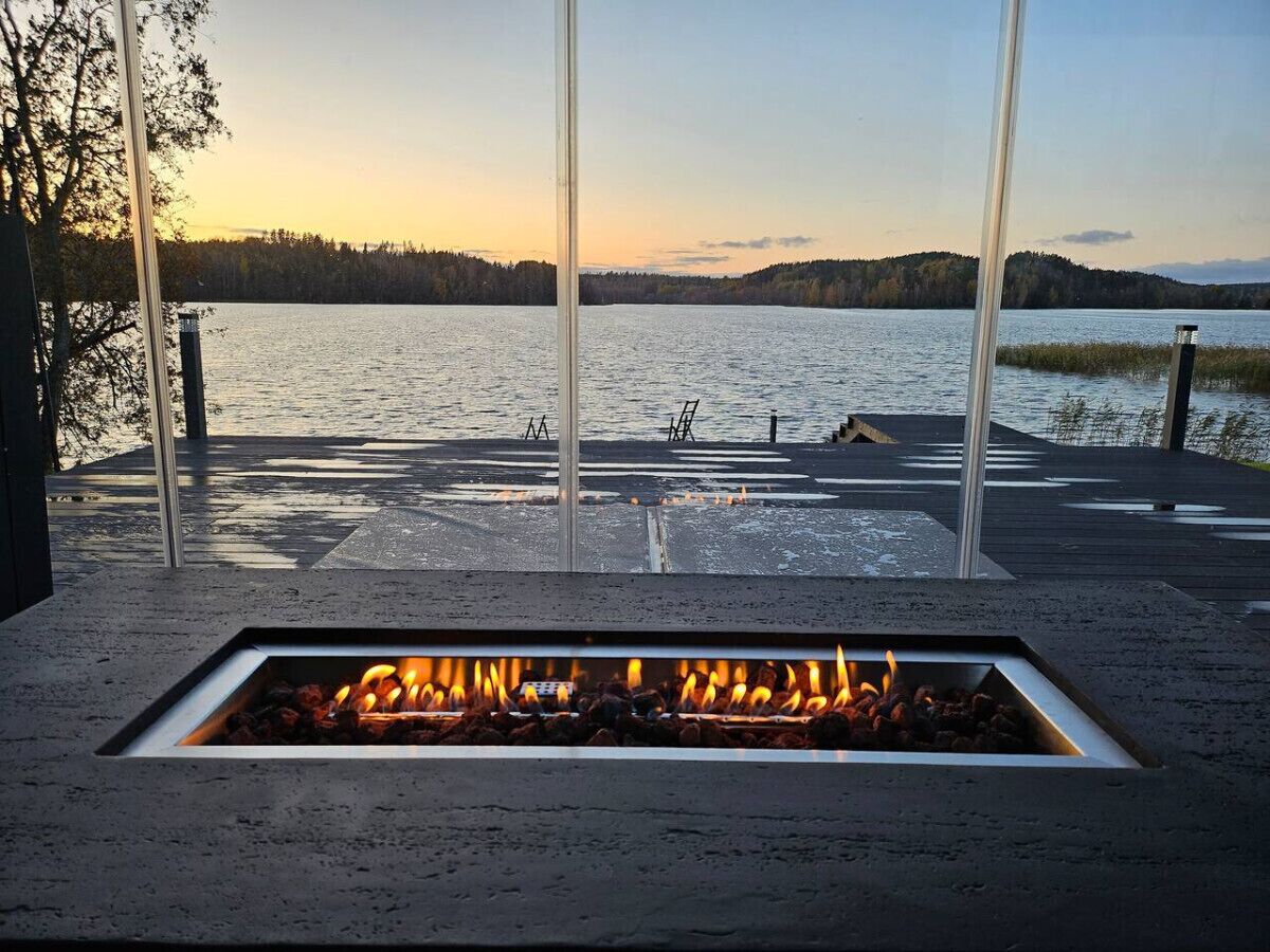 A fire pit with a view of a lake and forest at sunset.