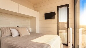 Ein Schlafzimmer mit einem Bett, Kissen, einem wandmontierten Fernseher und einer Schiebetür zu einem Balkon.