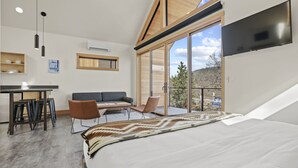 Un dormitorio moderno con una cama grande, un escritorio con taburetes, un sofá y un televisor montado en la pared.