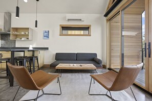 Ein modernes Wohnzimmer mit einer Couch, zwei Sesseln, einem Couchtisch und einer Küchenzeile mit Barhocker.