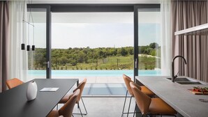 A modern kitchen with a large island, a dining area with a table and chairs, and a view of a swimming pool and greenery. - Villa Noble 1 with Spa (Bale)