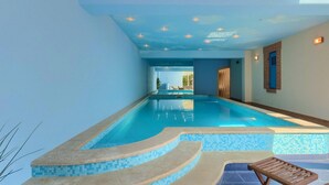 An indoor swimming pool with clear blue water, a tiled edge, and a wooden lounge chair. - Beach front home in Moscenicka Draga with WiFi (Moscenicka Draga)