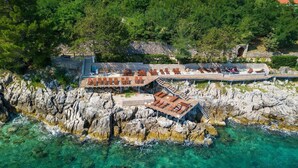 An aerial view of a coastal resort with a stone wall, wooden deck, and lounge chairs overlooking the sea. - Beach front home in Moscenicka Draga with WiFi (Moscenicka Draga)