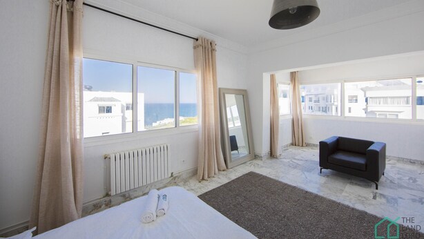 Un cuarto de hotel con cama, sofá, un ventanal con cortinas, un radiador y vista al mar.