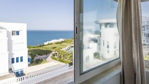 Una habitación con un ventanal grande con vistas a la costa, que ofrece una vista despejada del mar y edificios cercanos.