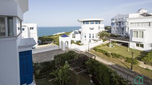 Un edificio moderno blanco con vistas al mar, un pequeño jardín y un cielo despejado.