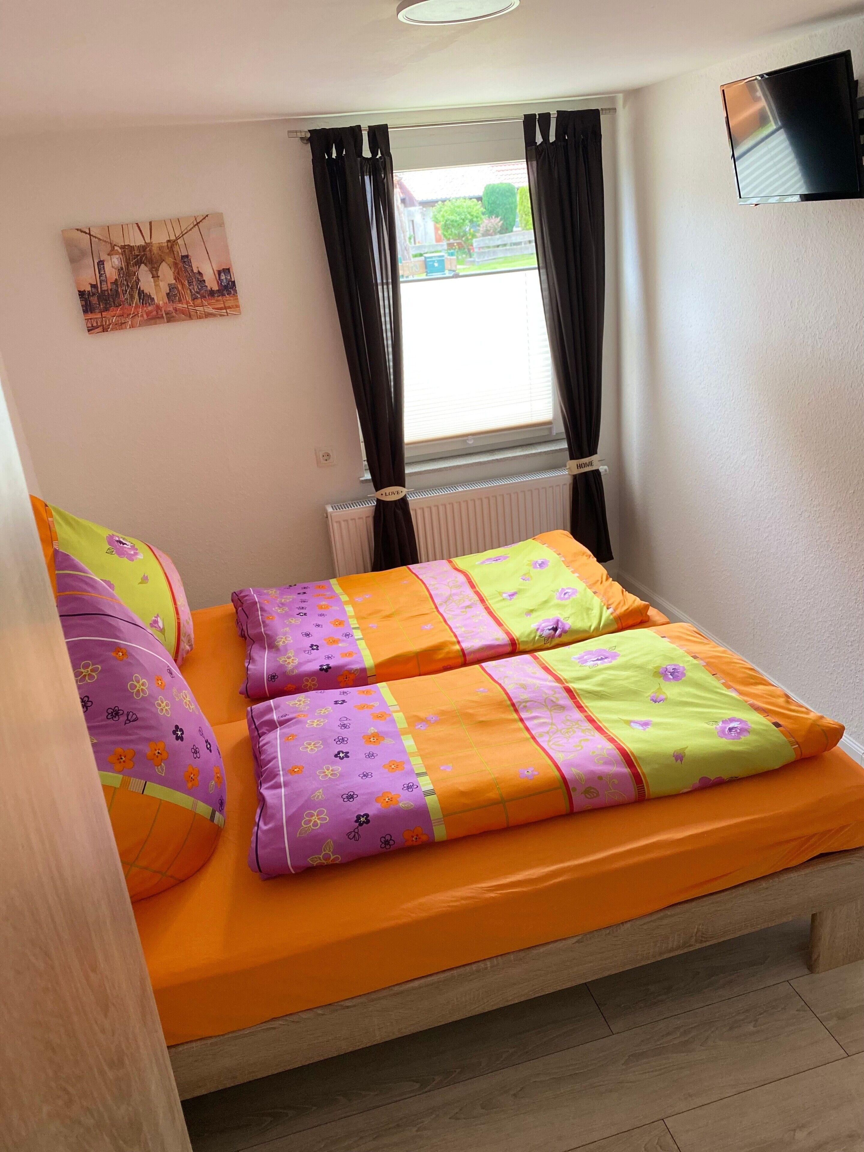 A bedroom with a bed, curtains, a flat-screen TV, and a radiator.
