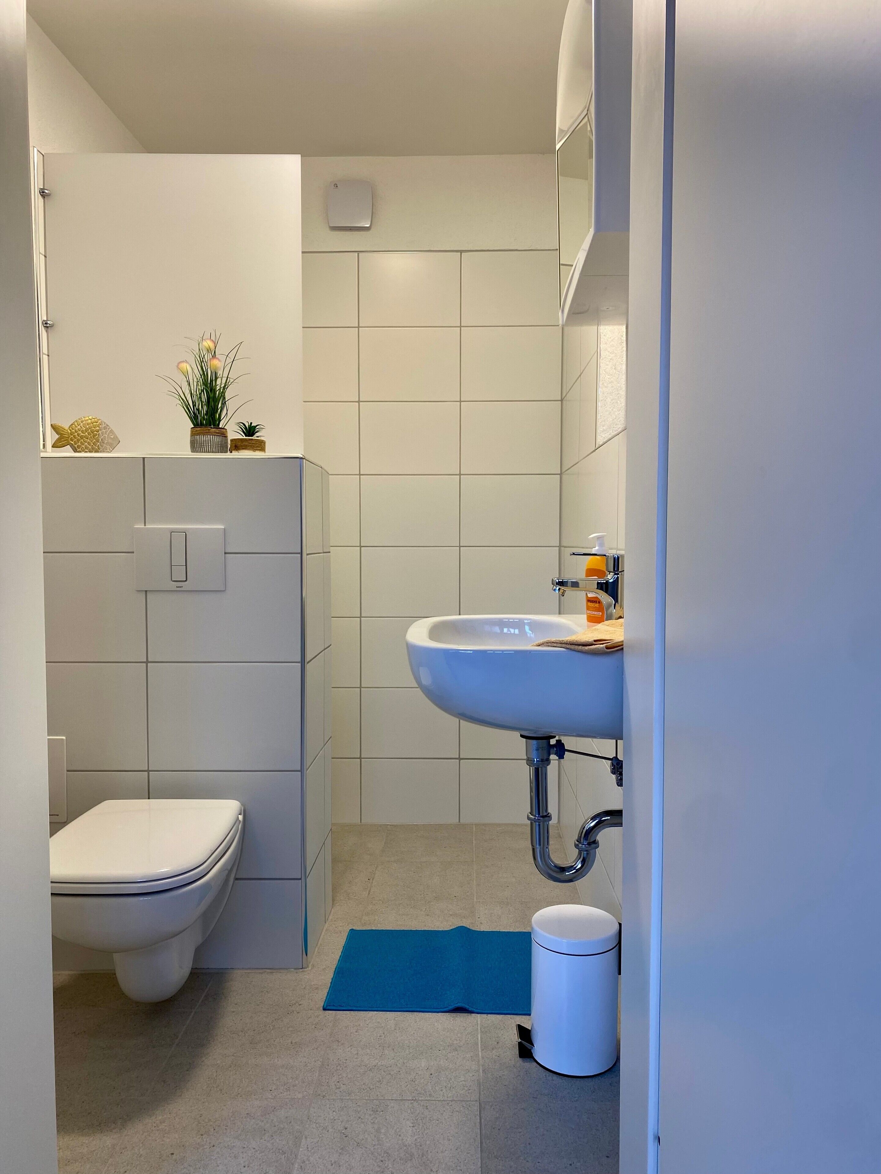 Ein Badezimmer mit Toilette, Waschbecken und einer kleinen Pflanze an der Wand.