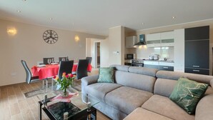 A modern living room with a grey sofa, a dining table with chairs, and a kitchen area with cabinets and appliances. - Lovely home in Motovun (Motovun)
