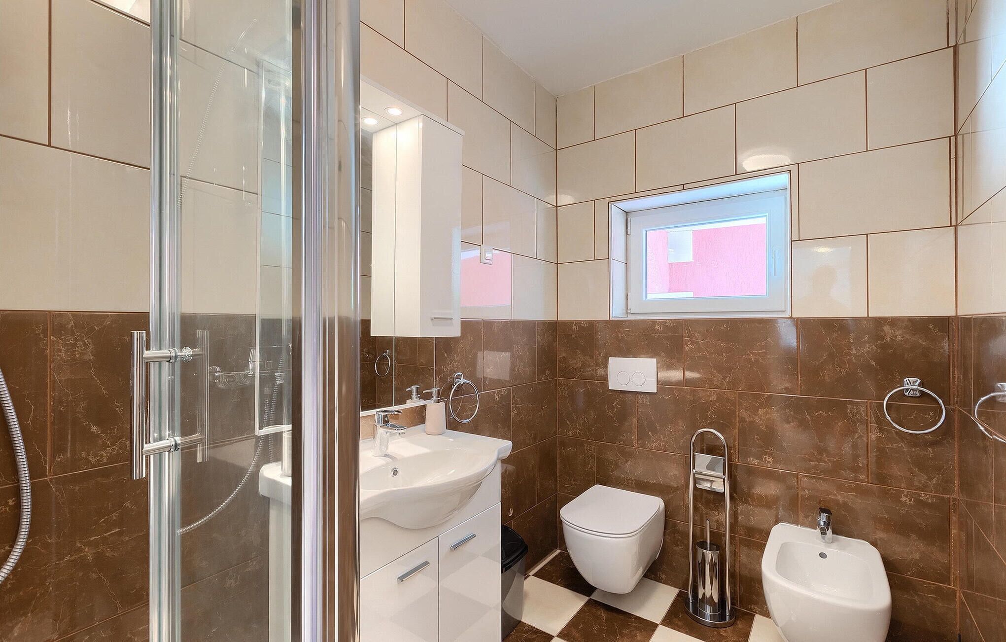 A modern bathroom with a glass shower enclosure, a white sink, a toilet, and a bidet.