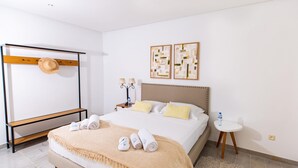 Hotelkamer met een bed, een houten rek met een hoed, twee wandlampen en twee abstracte schilderijen in lijsten.