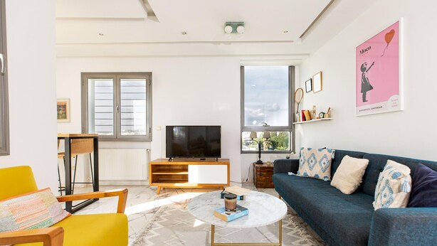 Een moderne woonkamer met een bank, een salontafel, een televisie en een raam met zonwering.