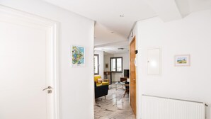Een gang met een witte deur, een radiator en een ingelijst kunstwerk aan de muur.